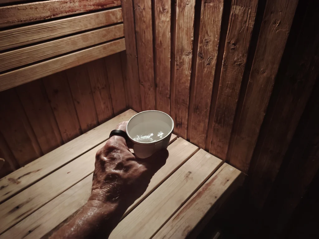 a hand holding a paper cup of water inside a traditional sauna with Oura Ring 5 on finger