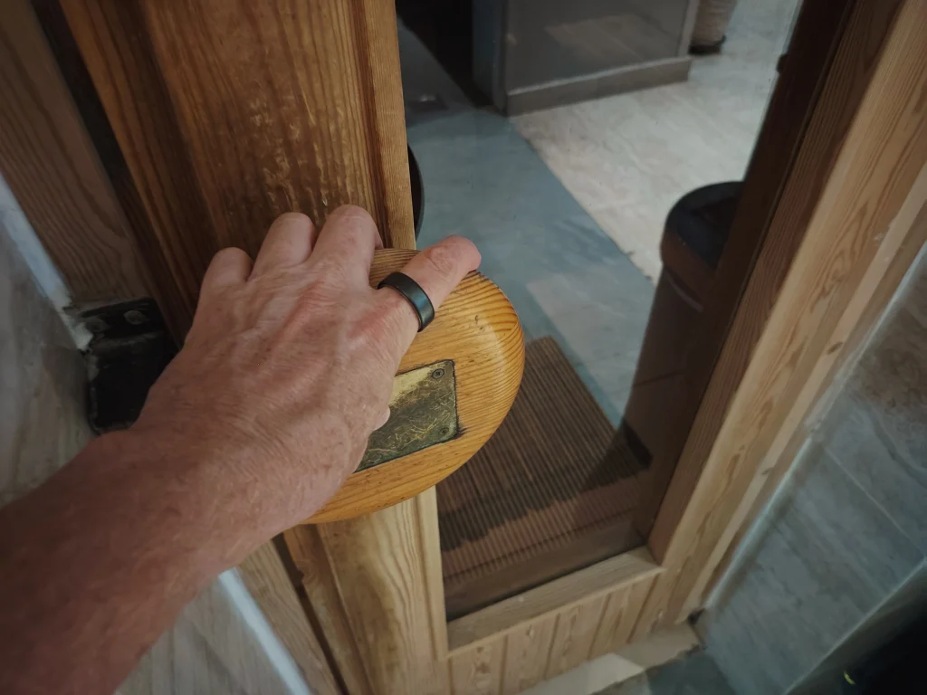 hand on Finnish sauna door with Oura Ring 5 on index finger